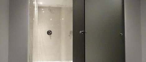 Une salle de bain moderne avec une douche à l’italienne en verre, une porte sombre et un sol carrelé.