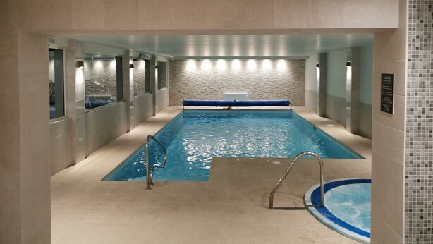 Una piscina interior con agua cristalina, un solárium azul y suelo de baldosas.