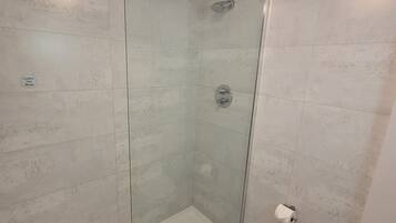 Une salle de bain moderne avec une douche à parois de verre, des toilettes et un panneau d’avertissement bien visible concernant l’eau chaude.