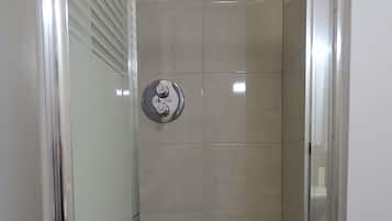 A glass-enclosed shower stall with a control panel and a ceiling-mounted showerhead.