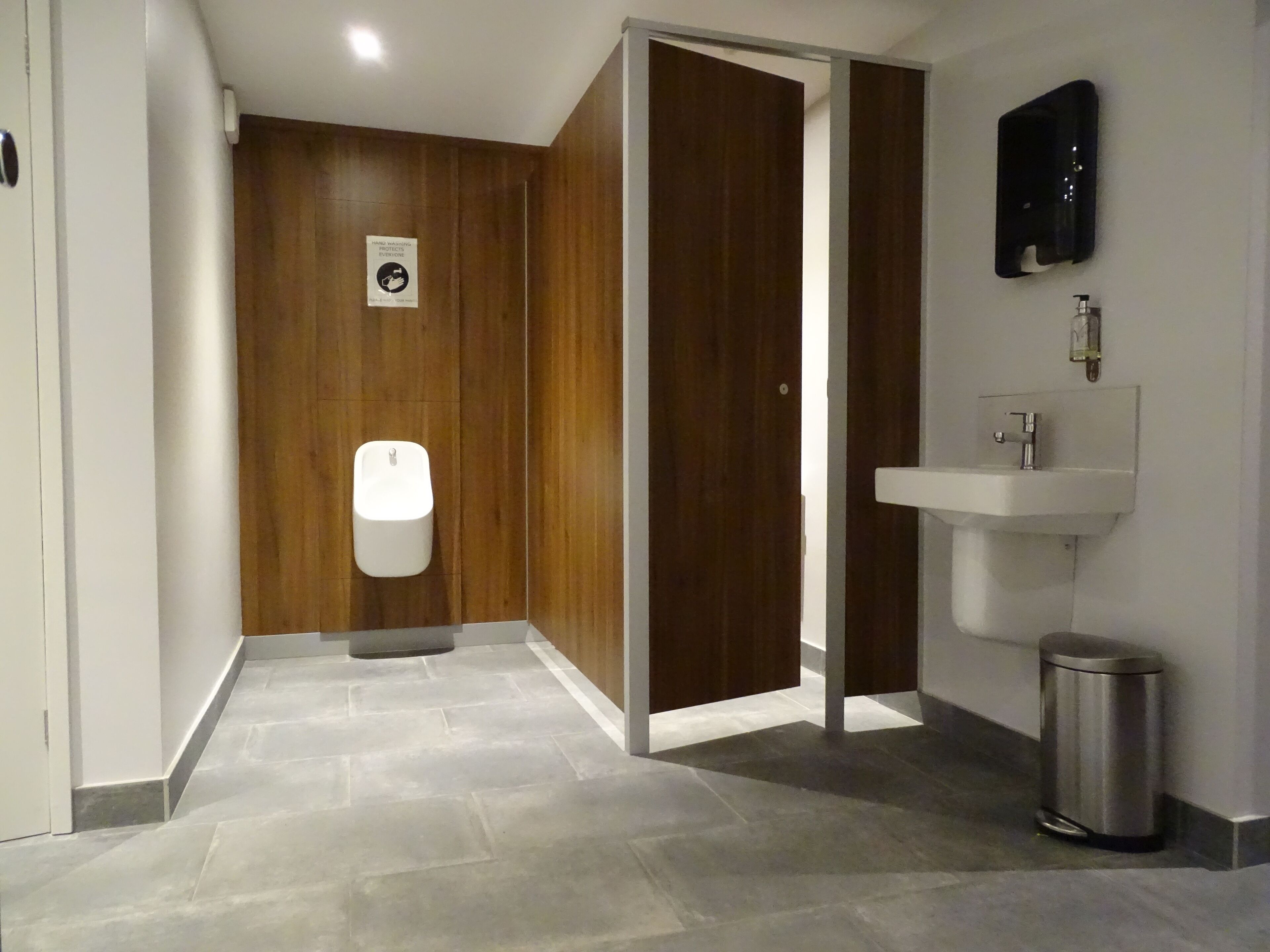 Un baño moderno con un separador de madera, un orinal blanco, un lavamanos y un cubo de basura.