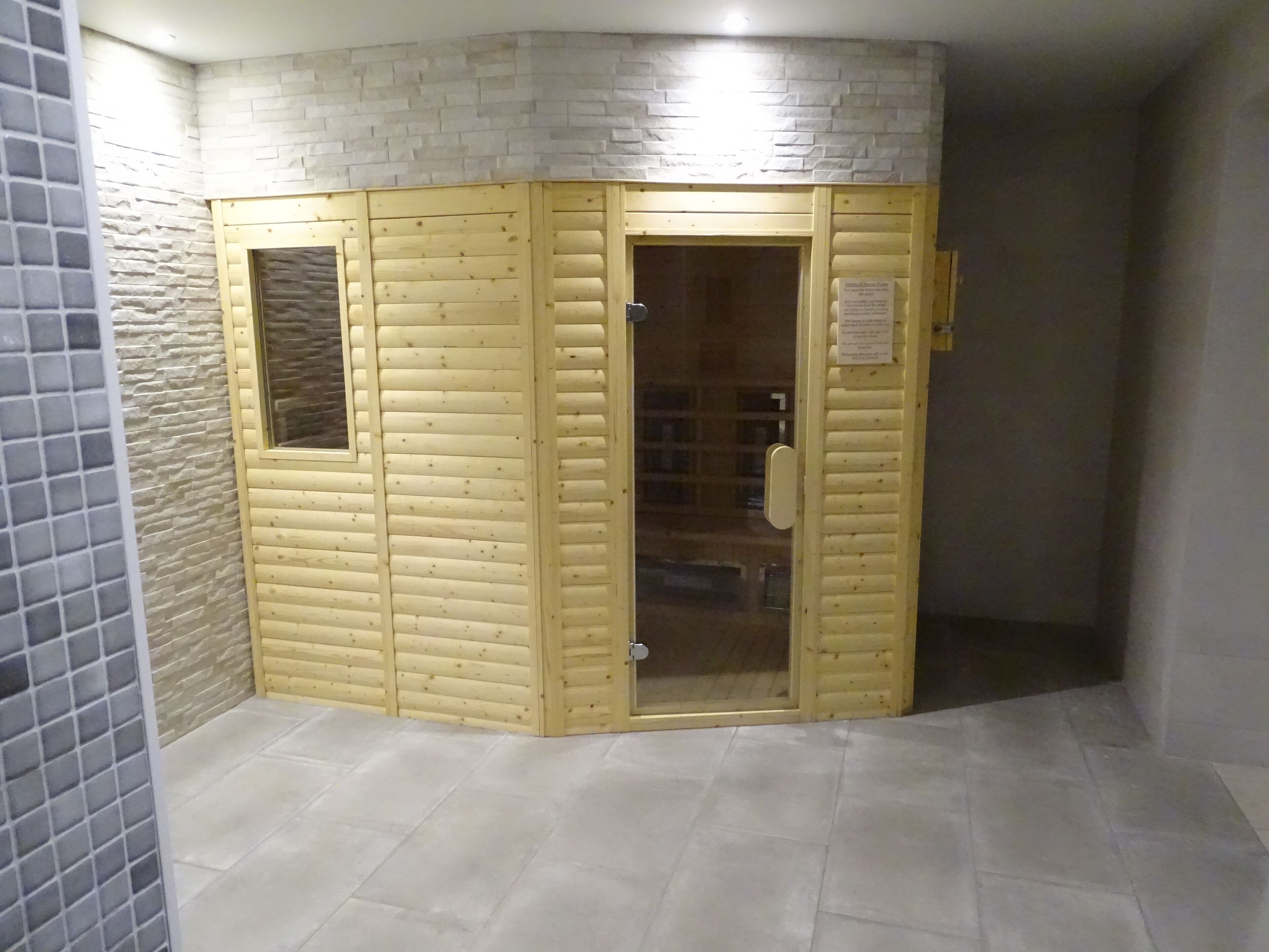 Una habitación de esquina con una puerta giratoria de madera, piso de baldosas y pared de ladrillo.