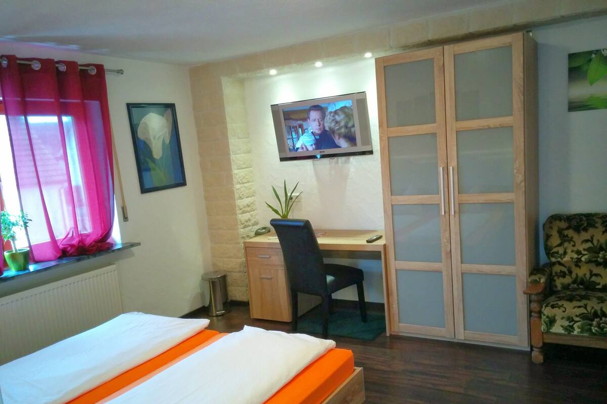 A bedroom with a bed, a desk, a chair, a wardrobe, and a television.