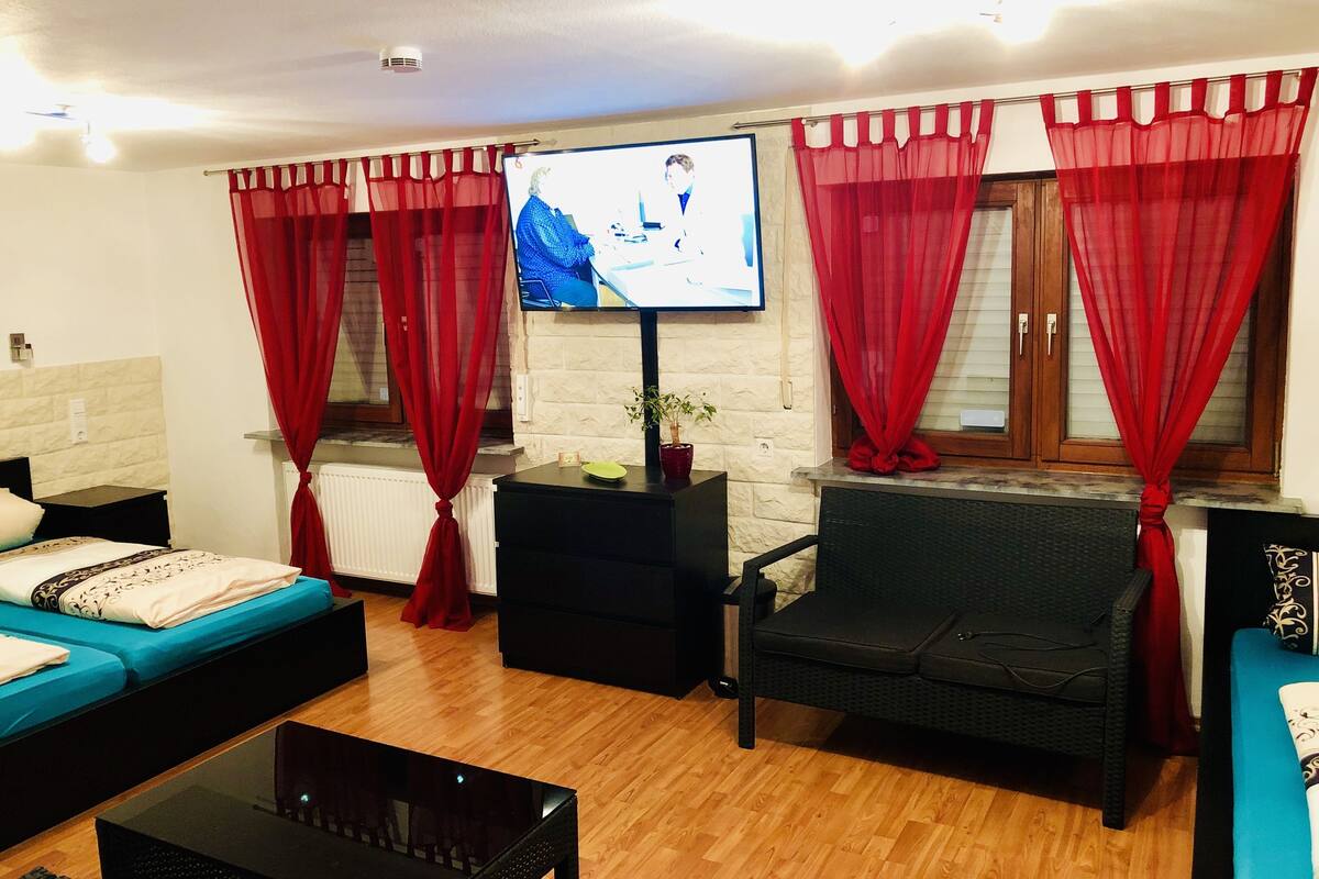 A living room with a sofa, a chair, a coffee table, a TV, and red curtains.