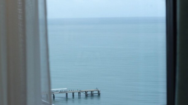 A view of a pier extending into calm water, viewed through a window with a partial view of a building's interior. - KNJZ Seaview Apartment (Batumi)