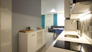 A modern kitchen with white cabinetry, a built-in oven, and a sink. There is a dining area with a table and chairs in the background. - KNJZ Seaview Apartment (Batumi)