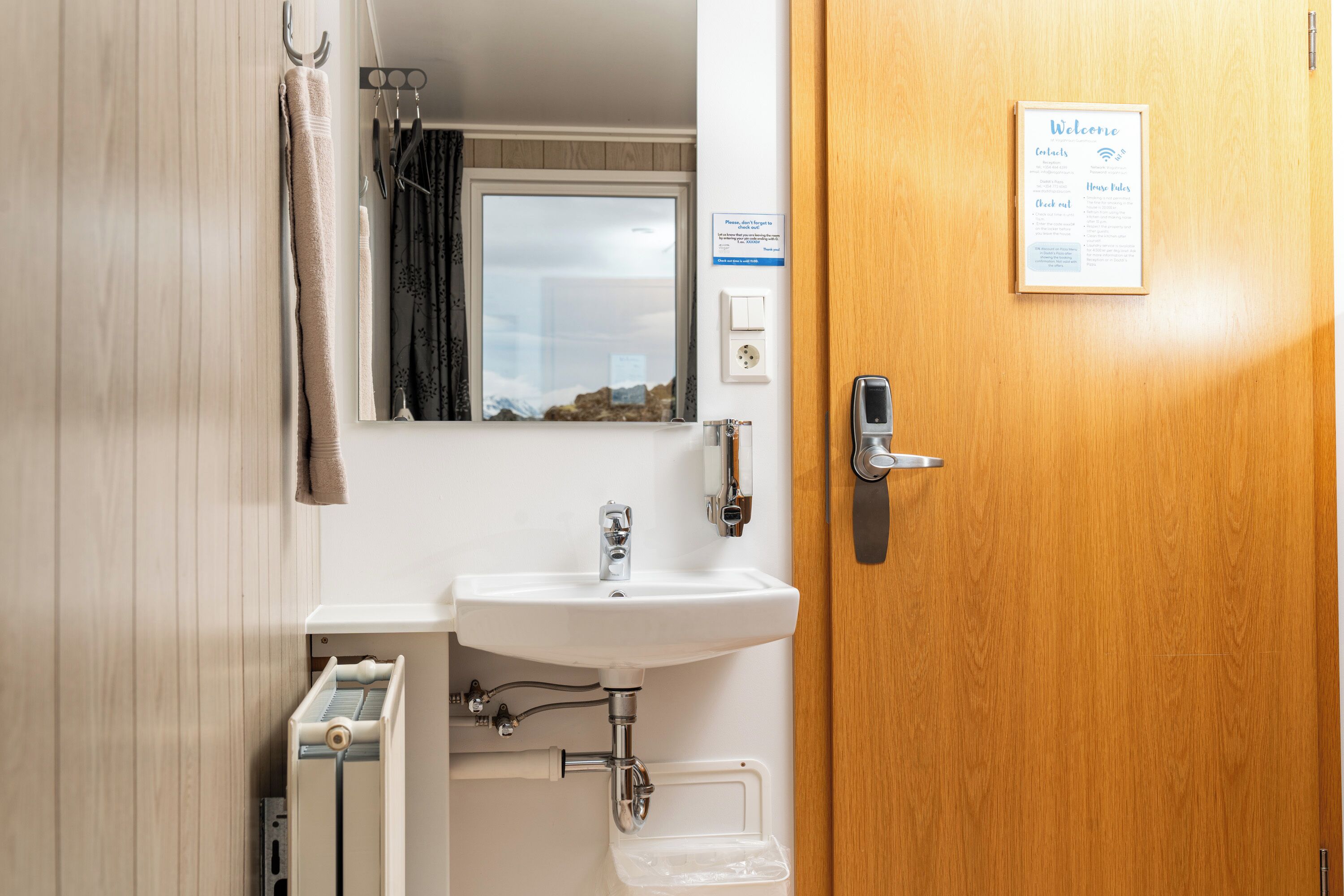 A bathroom with a sink, mirror, towel rack, and a wooden door with a welcome sign.