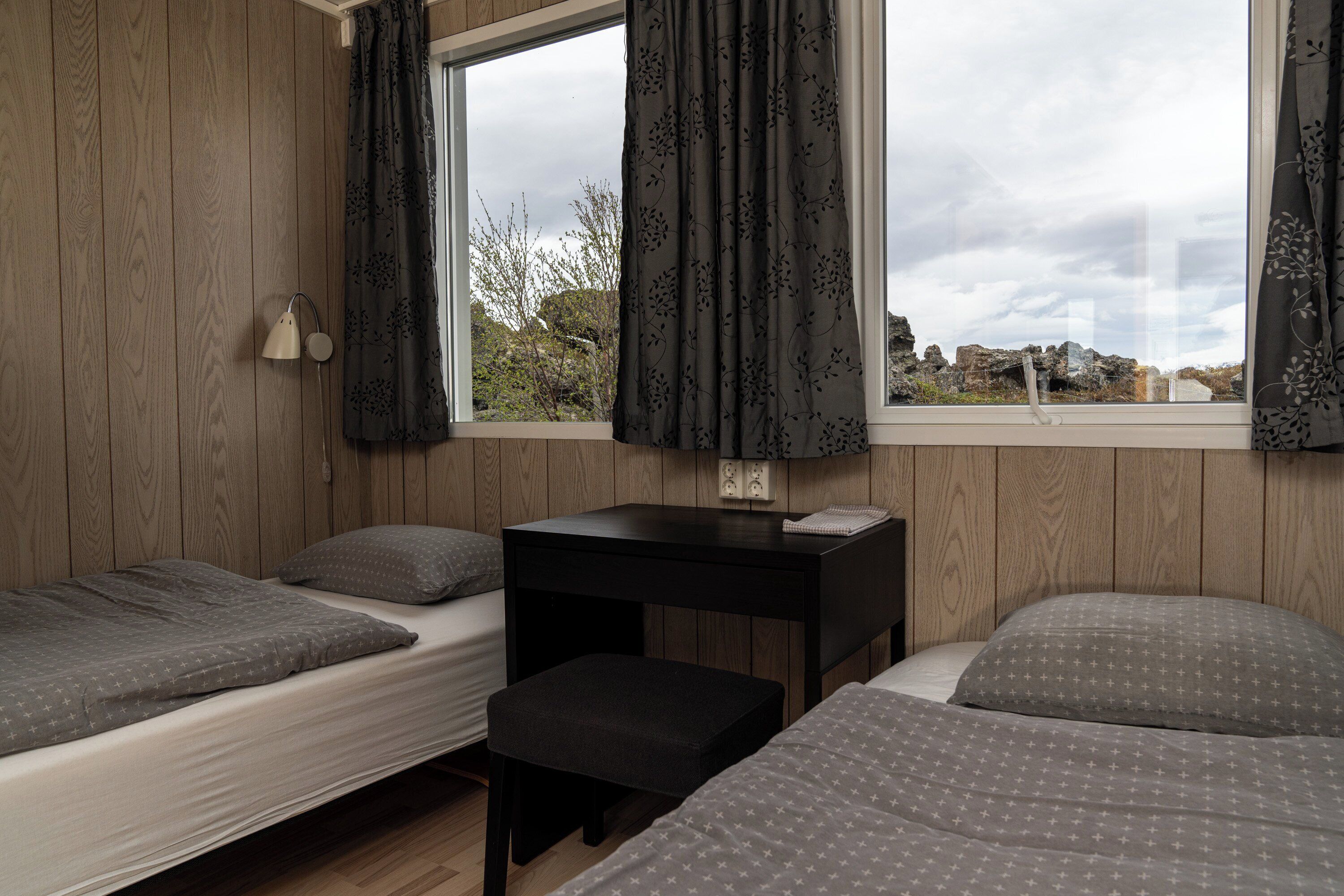 Una habitación con dos camas, una mesita y un ventanal con cortinas.