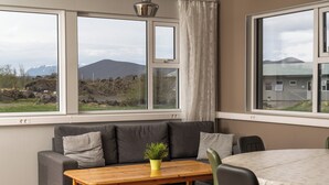 A room with a grey sofa, a wooden table with a plant, and a dining table with chairs. - Vogar Travel Service (Myvatn)
