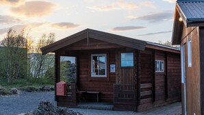 A wooden cabin with a porch, a small attached structure, and a gravel path leading to the entrance. - Vogar Travel Service (Myvatn)