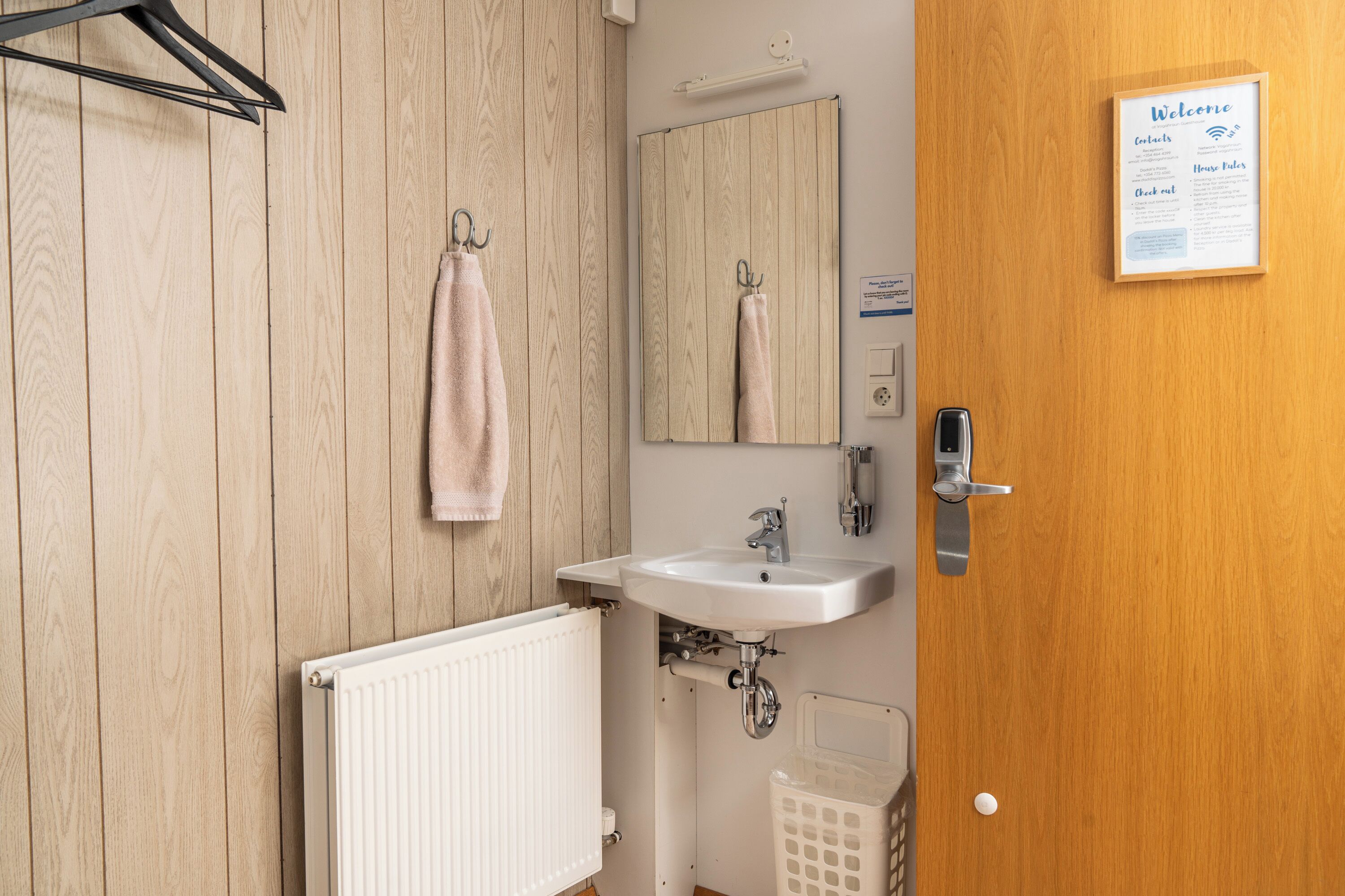 Een badkamer met een houten wand, een witte wastafel, een spiegel en een deur met een welkomstbord.