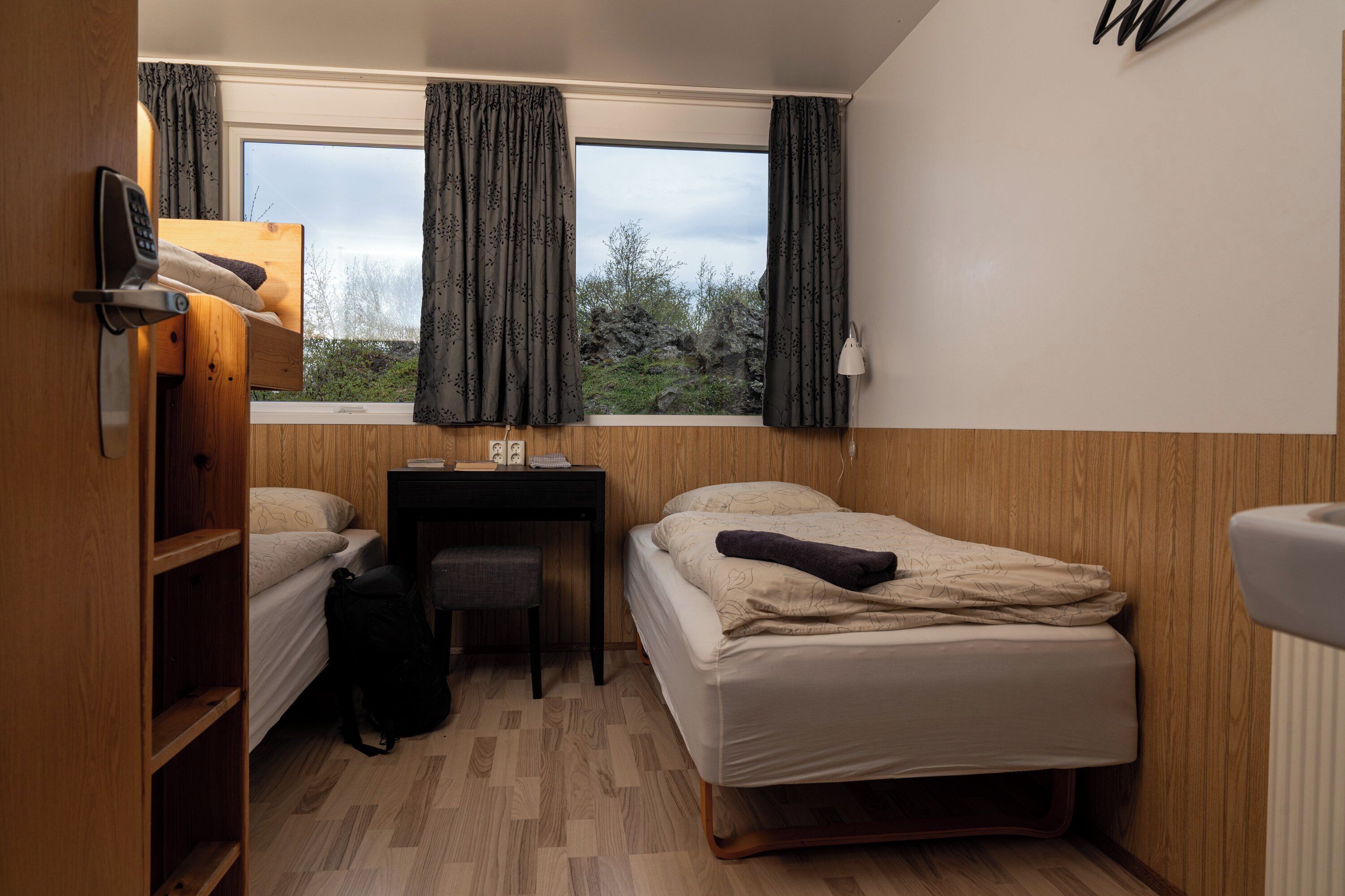 A compact room with two beds, a desk, and a window with curtains.