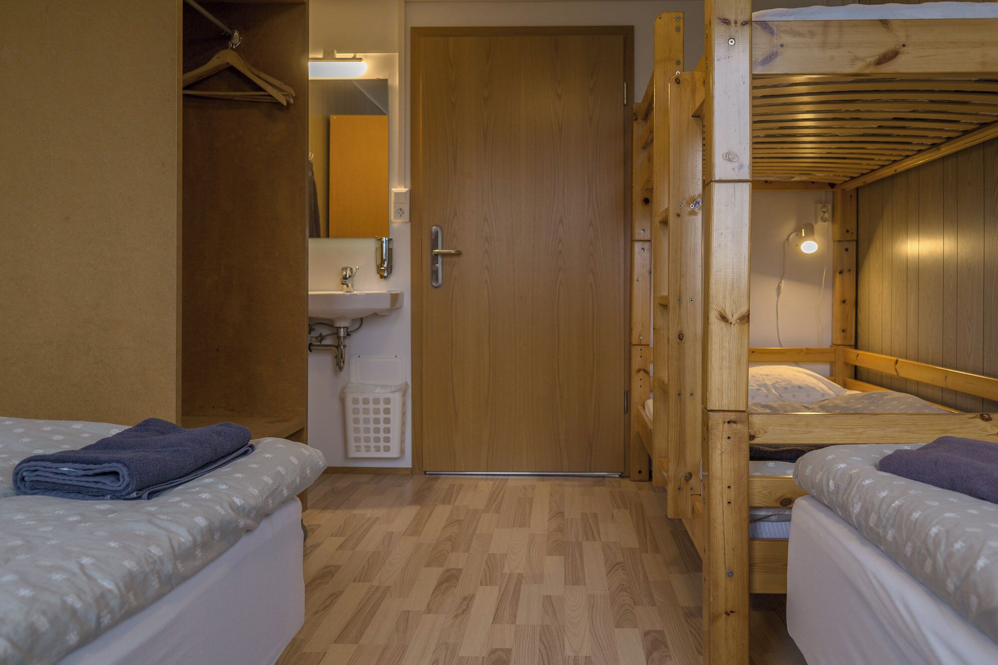 A compact room with two beds, a wooden ceiling, a sink, and a door.