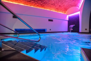 En indendørs swimmingpool med glasbund, metalstige og et vandfald.