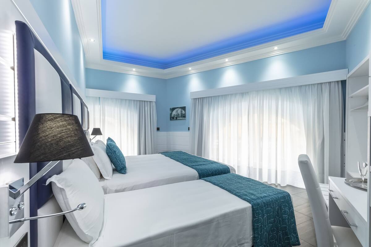 Et hotelværelse med to senge, et skrivebord, en stol, en lampe og en loftslampe.