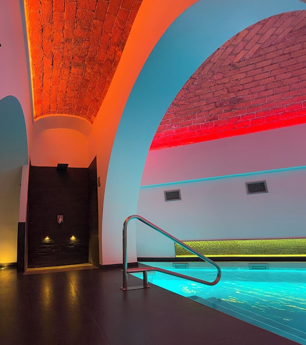 Un espace piscine intérieur moderne, doté d’un plafond incurvé, d’une rambarde métallique et d’un mur en briques.