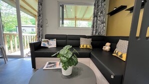 A modern living room with a black sofa, a round coffee table, and a potted plant. - Camping de Saulieu (Saulieu)