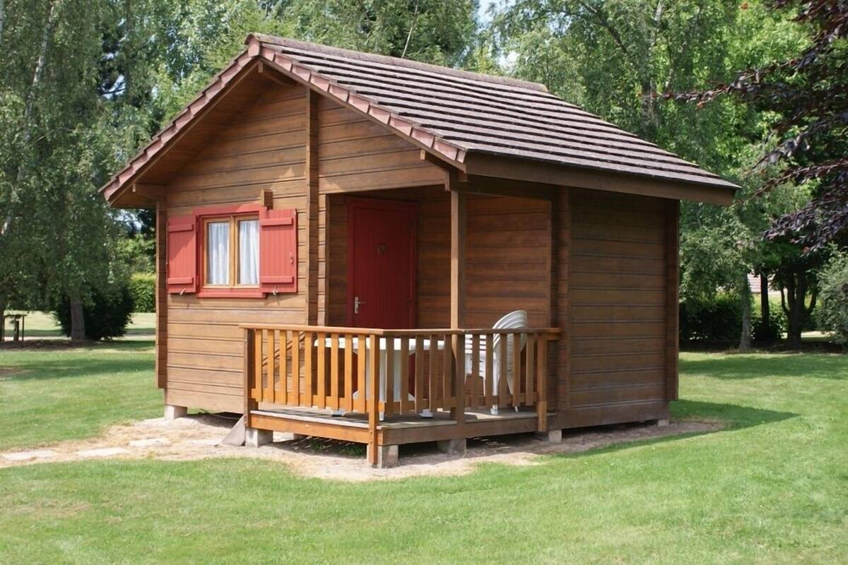 Eine kleine Holzhütte mit einer Veranda, einer roten Tür und einem Fenster mit Fensterläden.