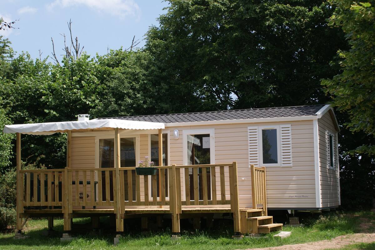 Ein kleines, eingeschossiges Mobilheim mit überdachter Veranda und einer kleinen Terrasse.