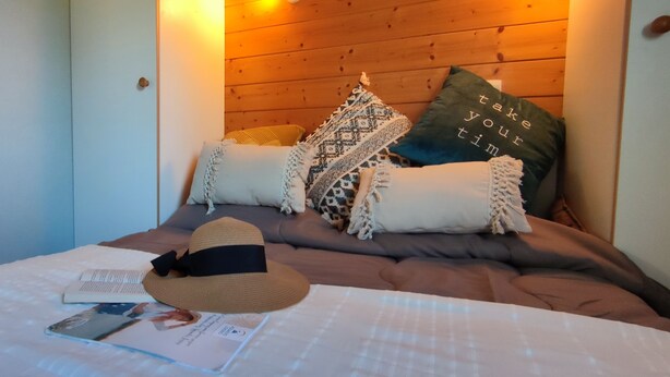 A cozy bedroom with a wooden headboard, a bed with a patterned throw, and a hat on the bed. - Camping de Saulieu (Saulieu)