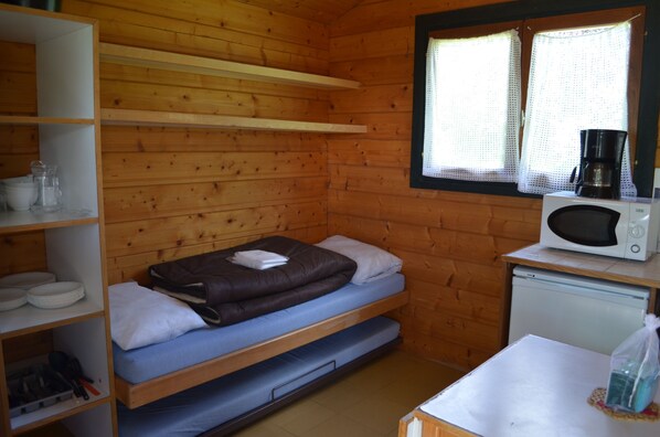 Una habitación de cabaña de madera, pequeña y acogedora, con literas, un microondas, una mesita y una ventana con cortinas.