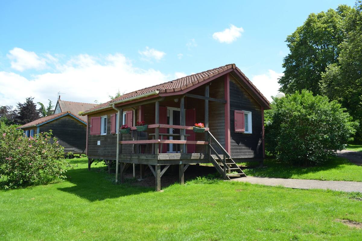 Ein Holzhaus mit Veranda und kleiner Terrasse, umgeben von viel Grün.