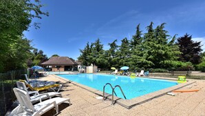 A swimming pool with lounge chairs and umbrellas, surrounded by trees and a building. - Camping de Saulieu (Saulieu)