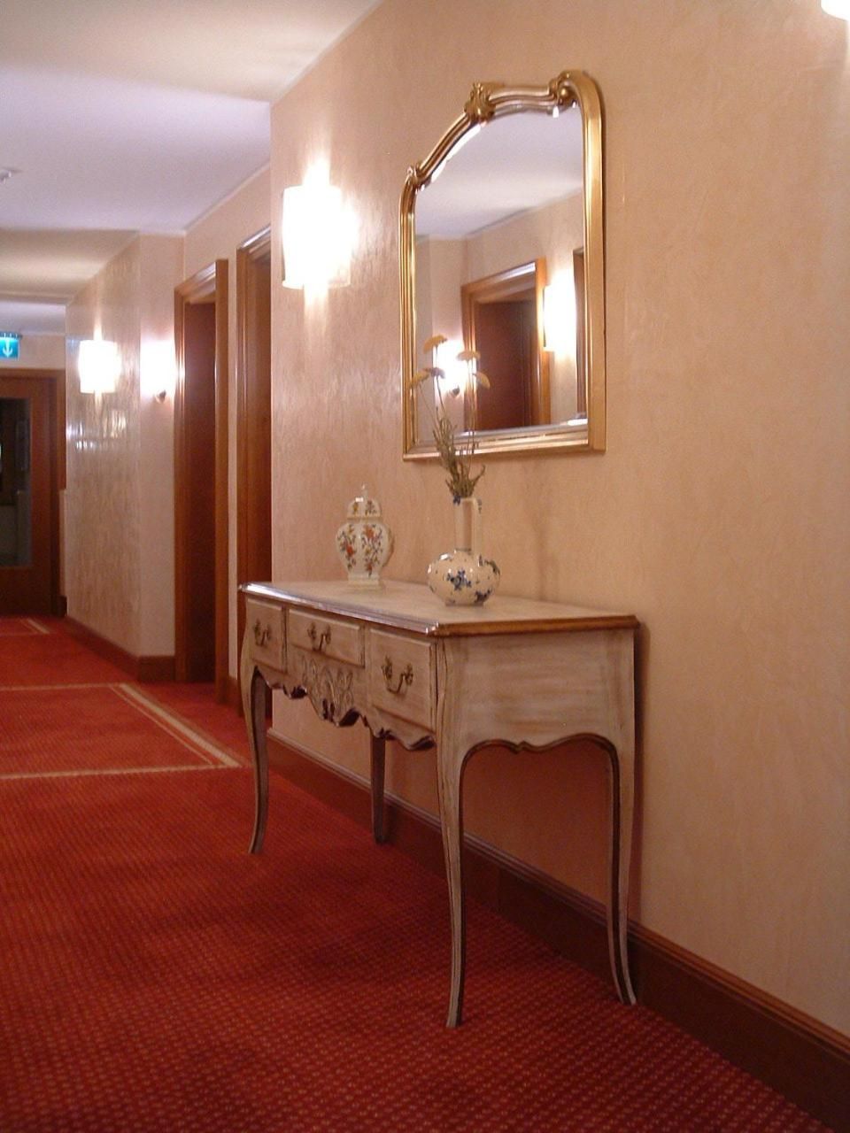 Un pasillo con alfombra roja, un espejo en la pared y una pequeña mesa con objetos decorativos.