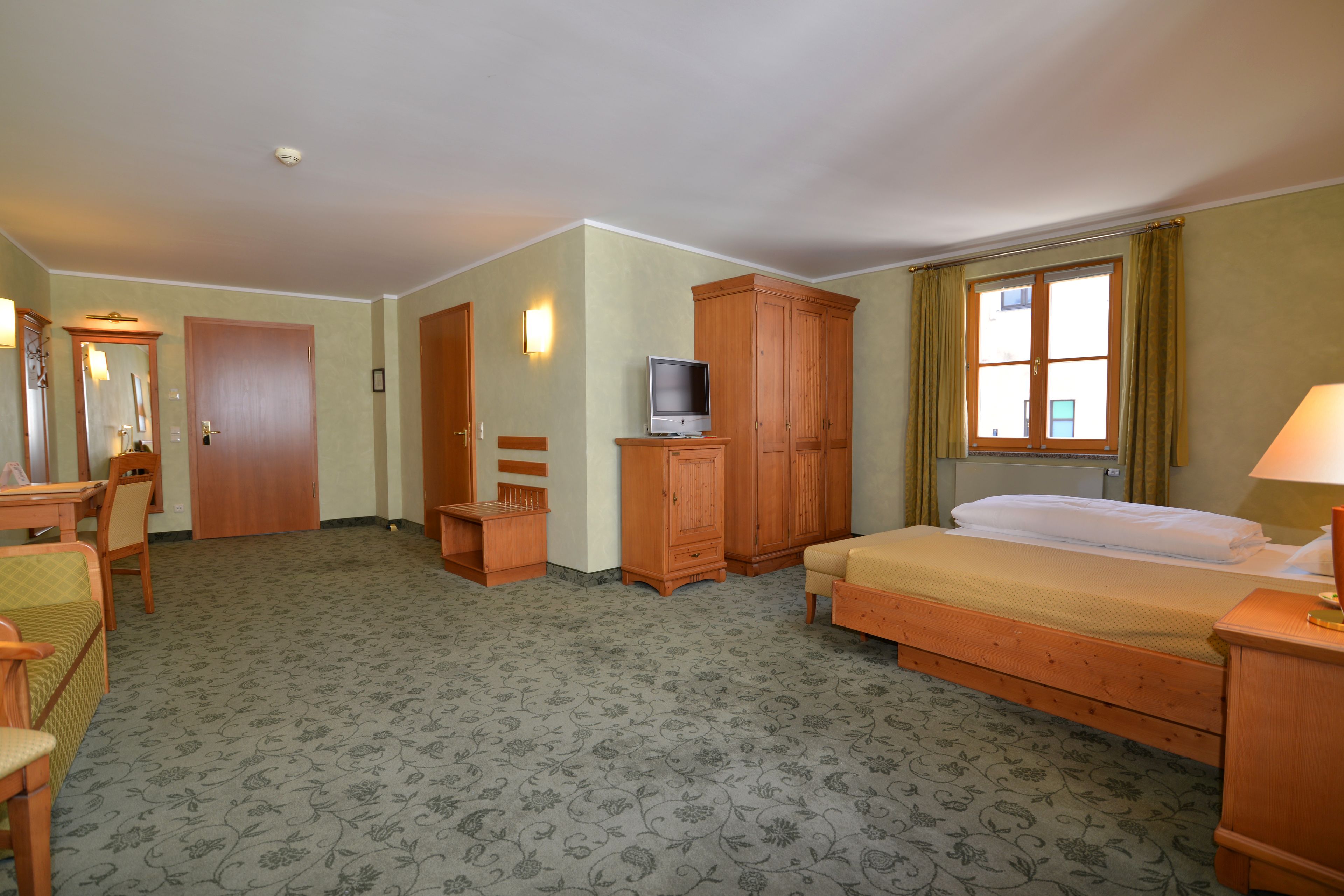 A hotel room with a bed, a television on a wooden stand, a desk with a chair, and a wardrobe.