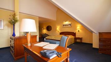 A hotel room with a desk, a telephone, a lamp, a bed, a chair, and a dresser.