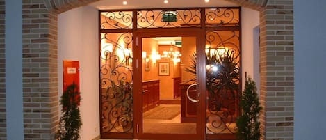 L’entrée d’un hôtel, avec une façade en briques, des grilles en fer forgé décoratives et des plantes en pot.