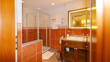 Un baño con cabina de ducha de vidrio, un lavabo con encimera de mármol y un espejo con marco dorado.