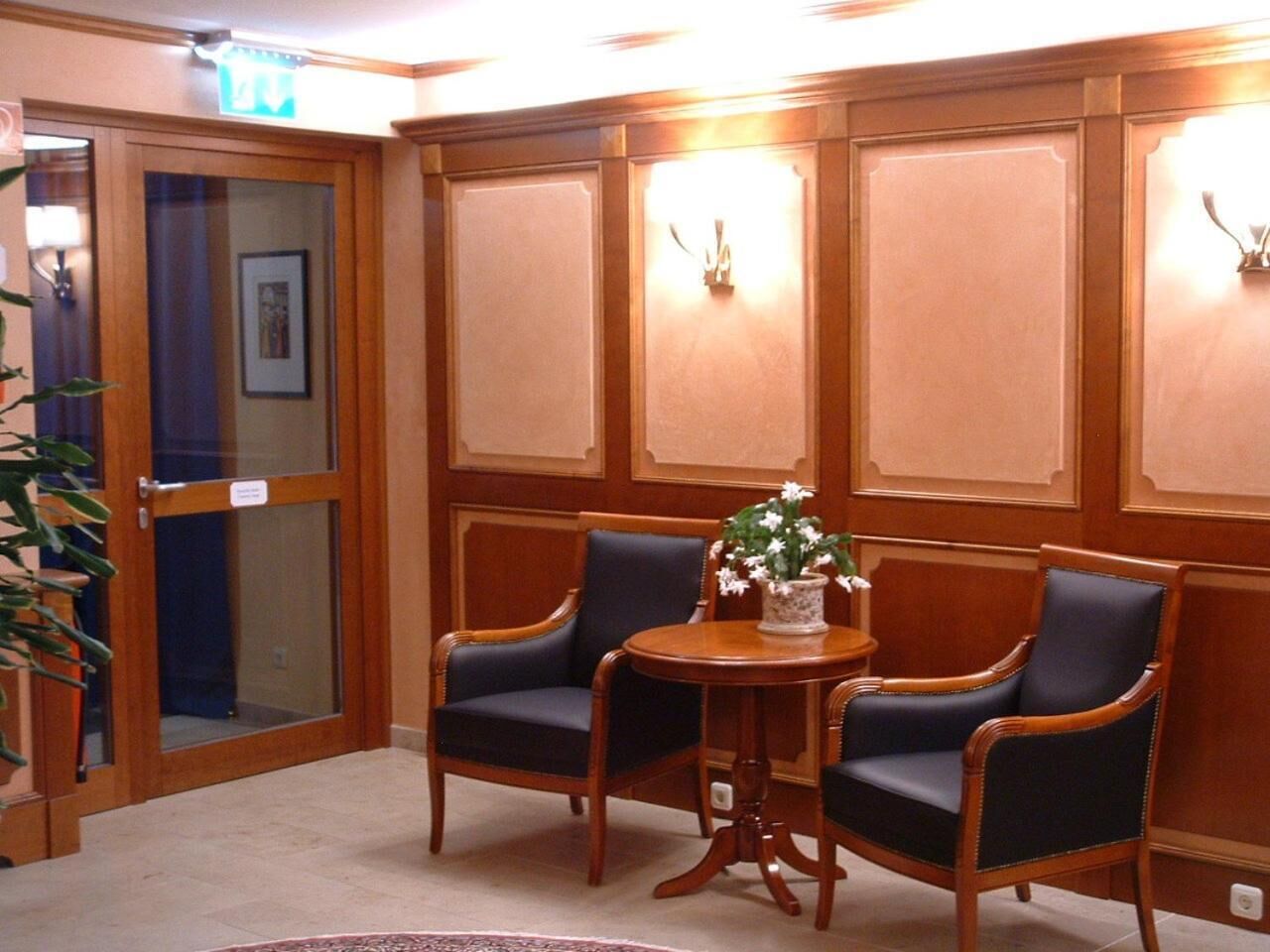 A room with two dark blue upholstered chairs, a round wooden table with a floral centerpiece, and wooden paneled walls.