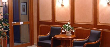 A room with two dark blue upholstered chairs, a round wooden table with a floral centerpiece, and wooden paneled walls.