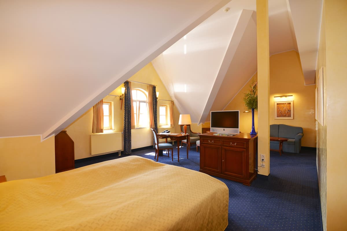 A hotel room with a large bed, a desk with a chair, a television, and a couch.