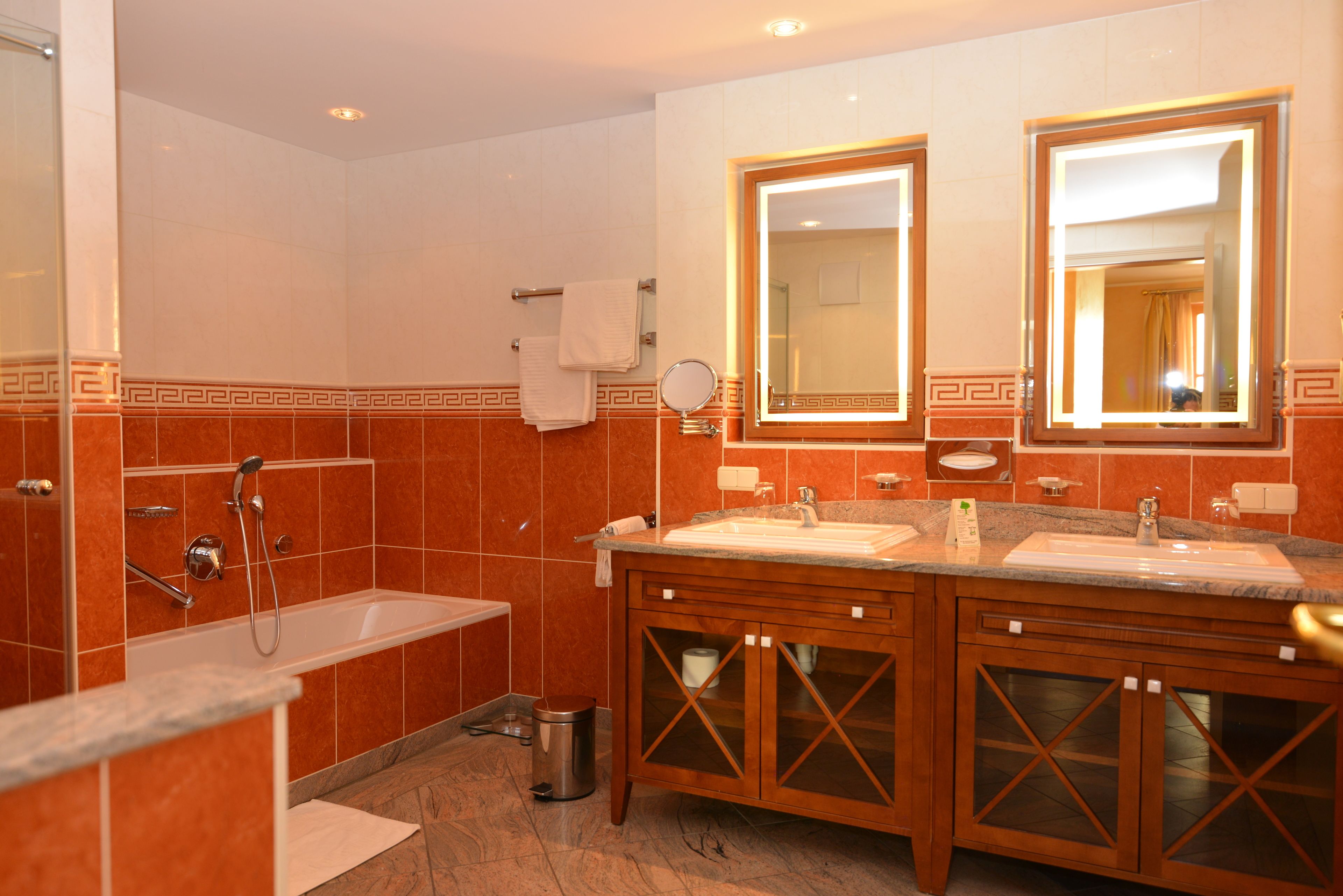 Un baño moderno con bañera, dos lavamanos y un mueble de tocador con puertas de vidrio.
