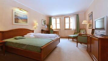 Una habitación de hotel con una cama grande, un escritorio, una silla, un televisor y una ventana con cortinas.