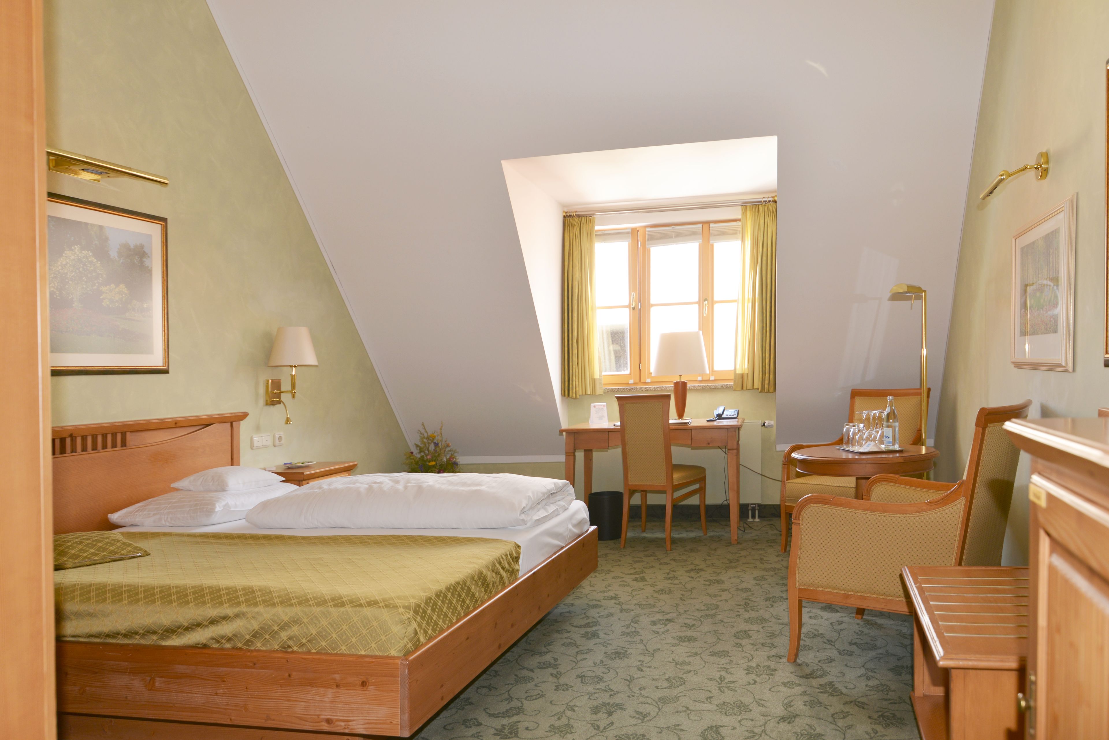Ein Hotelzimmer mit Bett, Schreibtisch, Stuhl und einem kleinen Tisch mit Lampe.