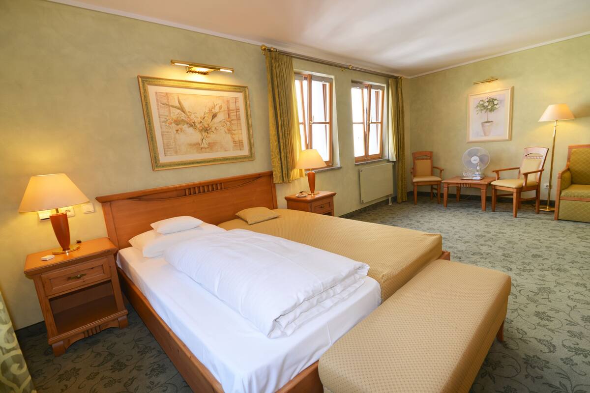 A hotel room with two beds, a wooden headboard, a nightstand with a lamp, a desk with a chair, and a framed picture on the wall.