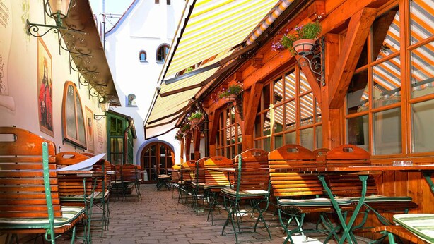 A narrow street with wooden benches and tables, white buildings, and a striped awning. - Altstadt Hotel Bräu Wirt (Weiden in der Oberpfalz)