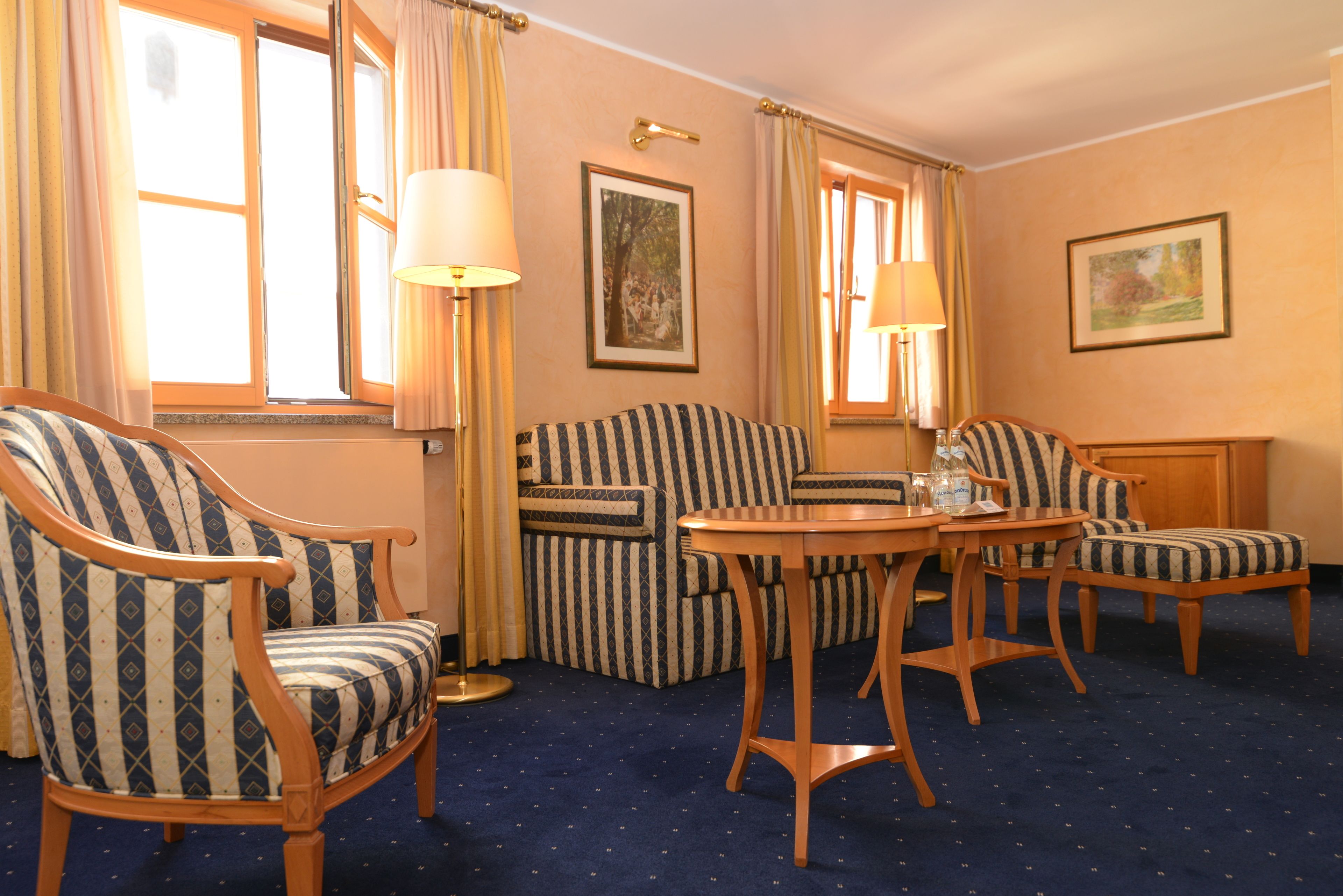 A hotel room with striped armchairs, a sofa, a round wooden table, and two lamps.