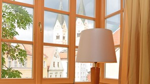 A room with a large wooden desk, a lamp, and a view of a church through large windows. - Altstadt Hotel Bräu Wirt (Weiden in der Oberpfalz)