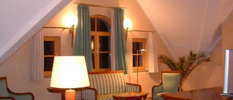 Une pièce mansardée chaleureuse, avec un plafond en pente, un canapé, deux fauteuils, une petite table et une lampe.