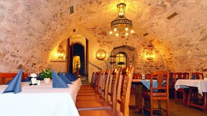 A restaurant with stone walls, wooden tables, and a chandelier. - Altstadt Hotel Bräu Wirt (Weiden in der Oberpfalz)