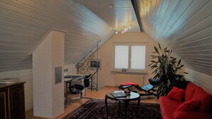 A cozy attic room with a sloped ceiling, a red sofa, a small table, and a staircase leading to an upper level. - Motel Residenz Labee (Weil am Rhein)