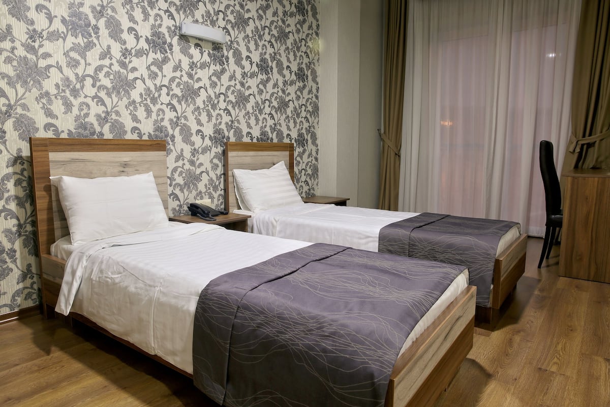 A hotel room with two wooden beds, white bedding, and a floral wallpaper pattern.