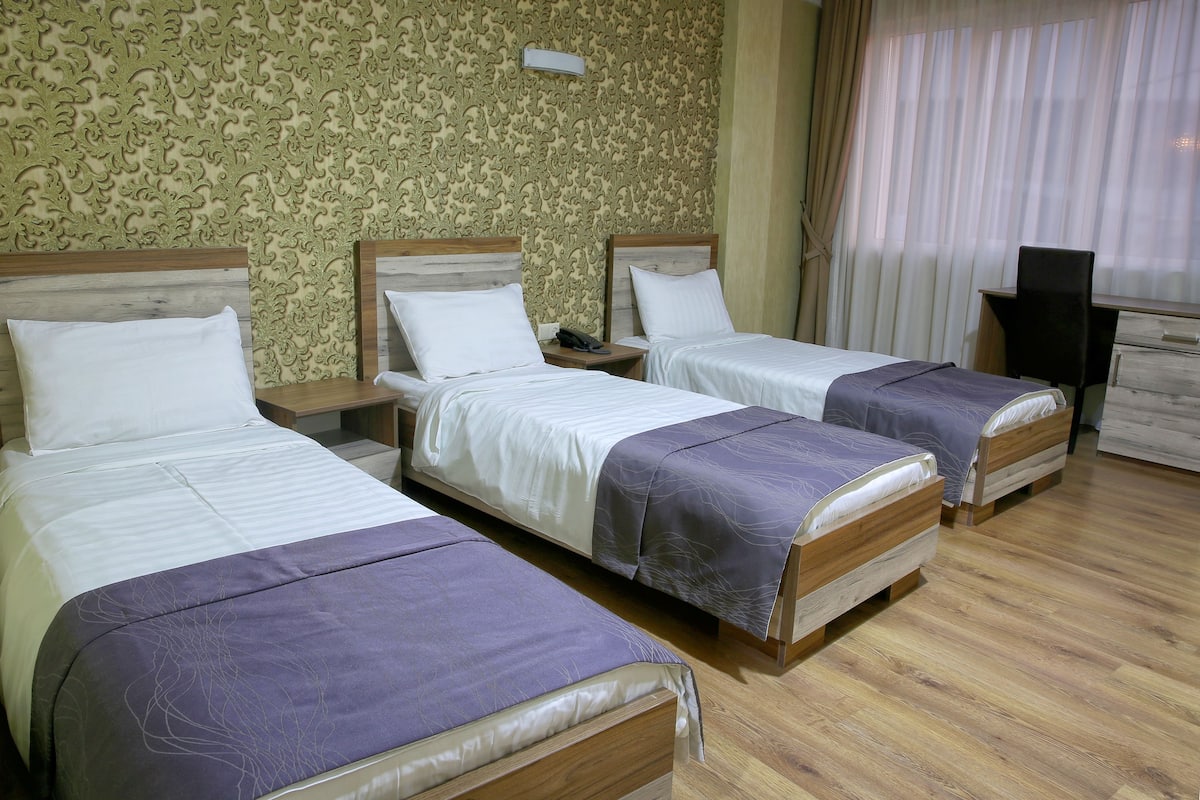 A hotel room with three single beds, wooden headboards, and a patterned wallpaper.