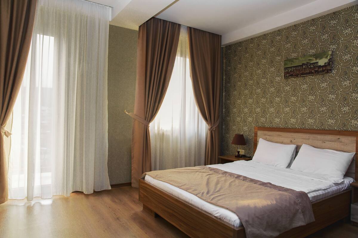 A hotel room with a wooden bed, a nightstand, and a painting on the wall.