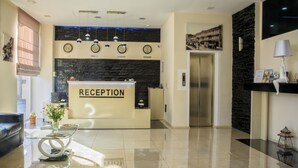 Zona de recepción con mostrador, una mesa de vidrio con un florero, pared de piedra negra e iluminación moderna.