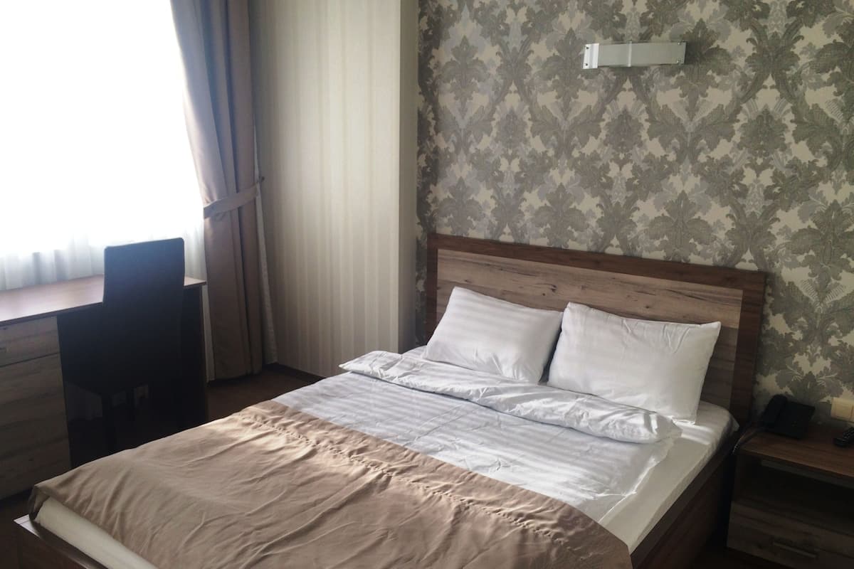 A neatly arranged hotel room with a bed, a desk, and a chair.